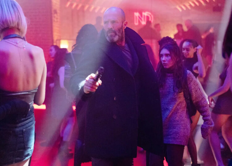 Jason Statham in Shelter. He is walking through a crowd and holding up a gun.