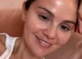Close-up of a person wearing a white tank top against a soft pink background.