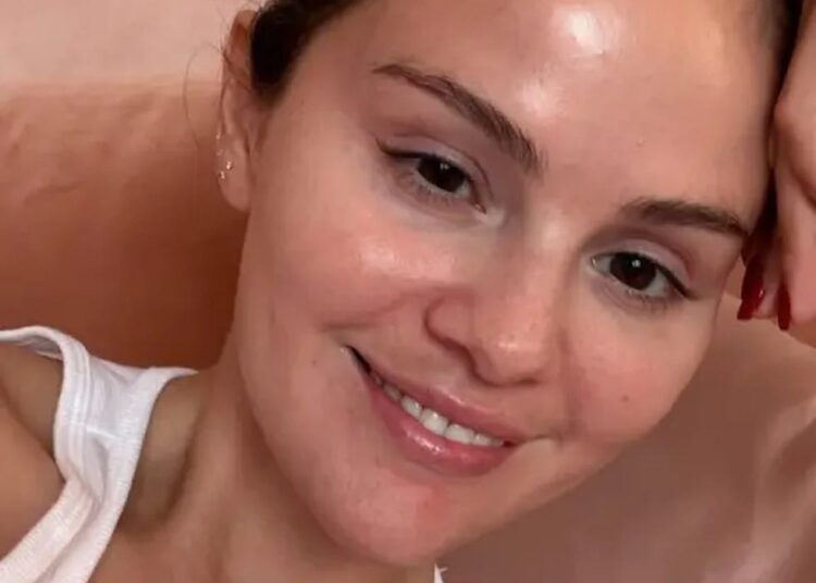 Close-up of a person wearing a white tank top against a soft pink background.