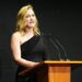 Kate Winslet in a black dress speaking from behind a lectern