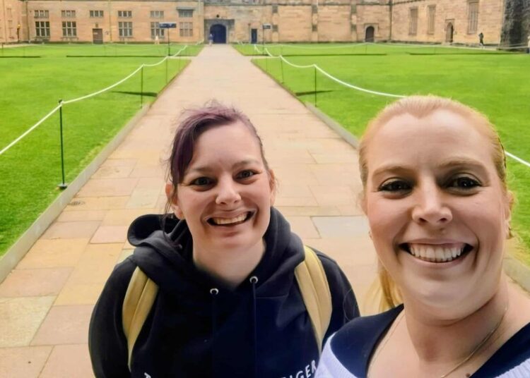 Lauren and Brianna take a smiling selfie in the middle of a university grounds.