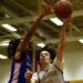 A basketball player tries to block the ball as a player on the opposing team shoots.