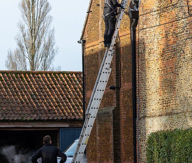 A Sky engineer up a ladder against the wall of Marsh Farm. The technicians were wearing uniforms with Sky VIP written on them