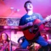 Late Developer Harrison Rimmer, singing emotively while playing the guitar, knelt on top of a human pyramid in The Fulford Arms, York.