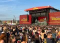 BBC An enormous crowd of people stand in front of a large stage. Massive red signs either side of the stage read 'Reading 25'. The sky is blue and largely cloudless and most of the people gathered are wearing summer clothes, with some wearing sunglasses and baseball caps.