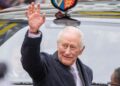 King Charles smiling and waving in front of a car