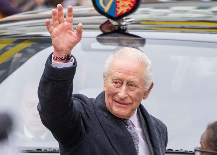King Charles smiling and waving in front of a car