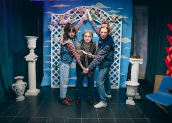 group of three people posing together in front of a decorative background with flowers