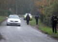 Two police cars, and several officers, can be seen near a road.