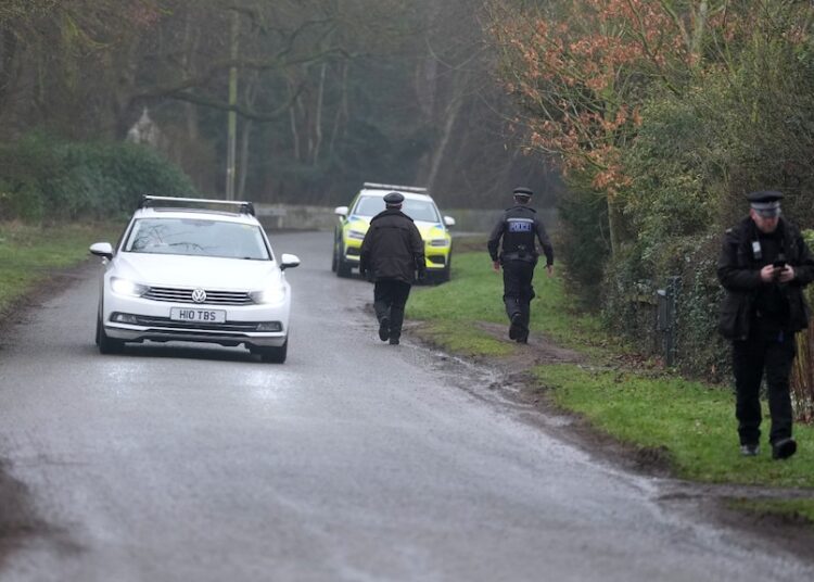 Two police cars, and several officers, can be seen near a road.
