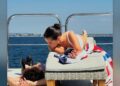 Two figures relaxing on a sunbed by the water.