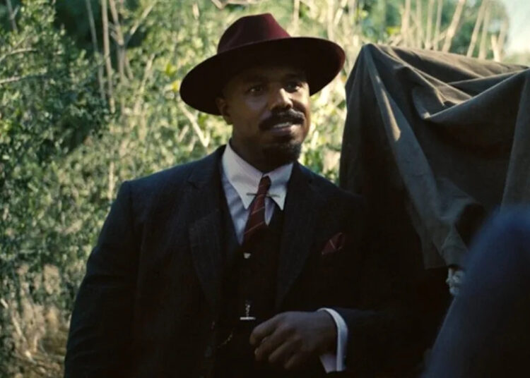 Michael B. Jordan leaning against a truck in Sinners. .