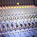 A professional music mixing console with numerous knobs and glowing indicator lights in a recording studio.