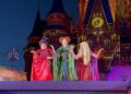 Three people in colorful witch costumes perform on stage at Mickey's Not So Scary Halloween Party in front of a castle.