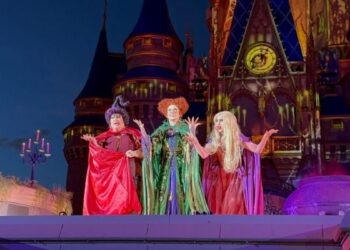 Three people in colorful witch costumes perform on stage at Mickey's Not So Scary Halloween Party in front of a castle.