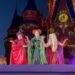 Three people in colorful witch costumes perform on stage at Mickey's Not So Scary Halloween Party in front of a castle.