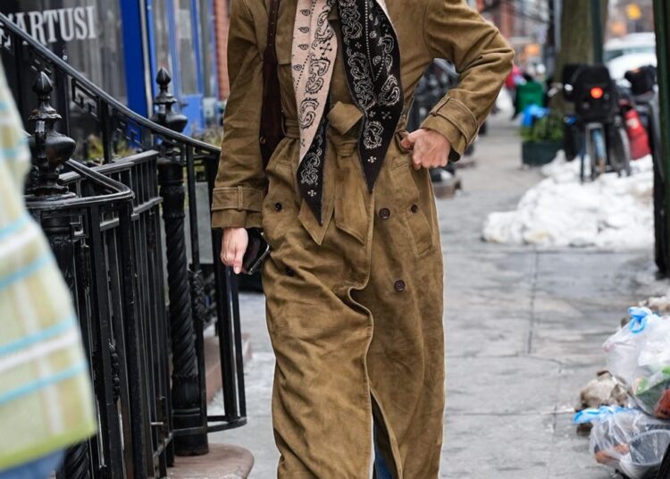 person walking on a city sidewalk dressed in a long coat and scarf