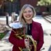 A white woman with blond hair holds a French horn in an outdoor photo. Anna Eberwine