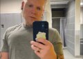 Blake Garrett wearing a gray t-shirt and holding a phone in front of him.