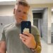 Blake Garrett wearing a gray t-shirt and holding a phone in front of him.