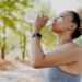 Photo of a woman drinking water from a plastic bottle in a green park surround by trees