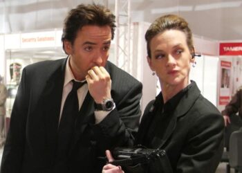 John Cusack as Brand Hauser and Joan Cusack as Marsha Dillon dressed all in black at an arms convention in War, Inc.