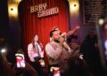 John Legend performing in front of a crowd of people with Kelly Clarkson and Druski.