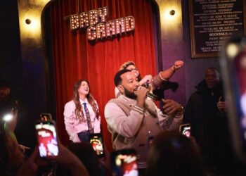 John Legend performing in front of a crowd of people with Kelly Clarkson and Druski.