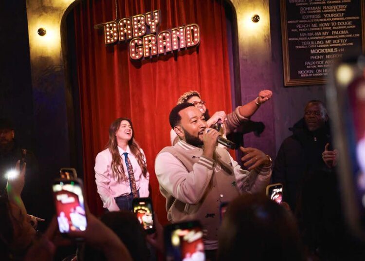 John Legend performing in front of a crowd of people with Kelly Clarkson and Druski.