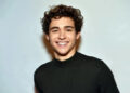 Celebrity wearing a ribbed sweater, smiling at the camera with curly hair styled casually