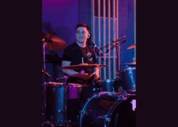 Asher playing the drums in a room lit by purple lights.