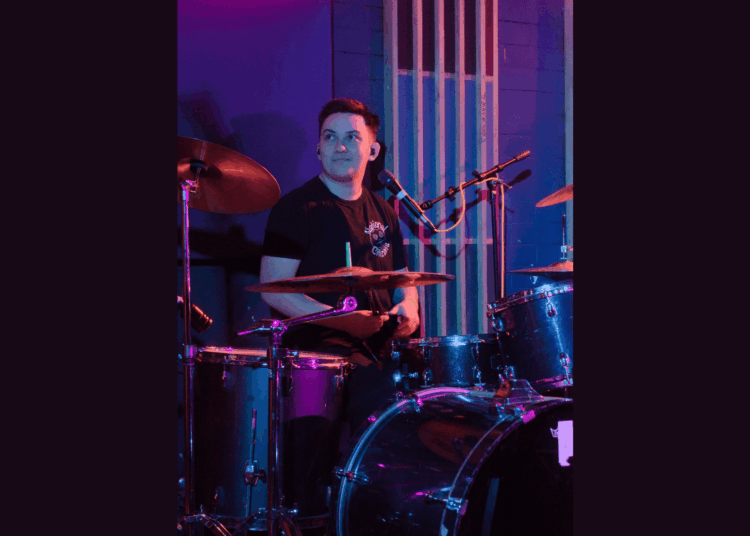 Asher playing the drums in a room lit by purple lights.