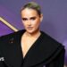 Moly-Mae Hague on a red carpet. Background is purple and gold and the social media star wears a black wide cut collared dress with her blonde hair scraped back.