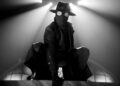 a character in a dramatic pose wearing a mask and fedora