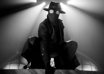 a character in a dramatic pose wearing a mask and fedora