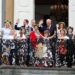 A group of people in formal attire standing on a balcony and waving