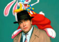 Bob Hoskins in a trench coat and hat with a cartoon rabbit in a colorful outfit perched on his shoulder