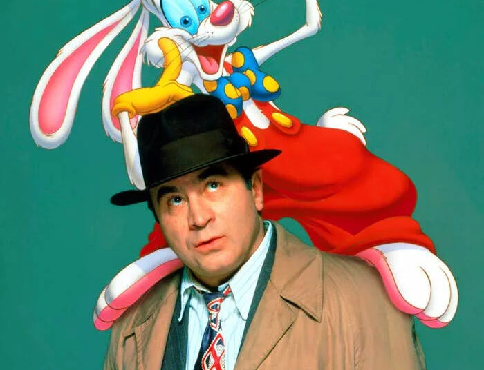 Bob Hoskins in a trench coat and hat with a cartoon rabbit in a colorful outfit perched on his shoulder