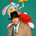 Bob Hoskins in a trench coat and hat with a cartoon rabbit in a colorful outfit perched on his shoulder