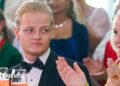 A young man with blond hair and a bow tie looks on as a woman in a yellow dress claps