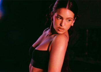 Rosalia posing in low light, wearing a black top.