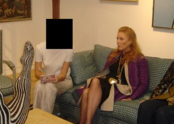 A woman sitting on a sofa looking on. Next to her, another woman is sitting, but her face has been redacted.