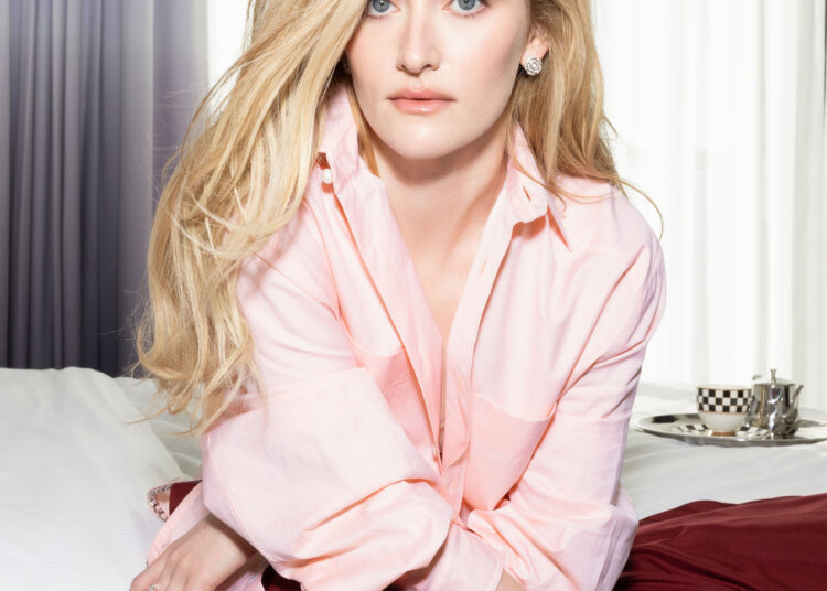 Sarah Pidgeon wearing a pink top and scarlet skirt in a hotel room