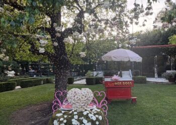 A decorated outdoor space with floral arrangements and a hot dog cart.