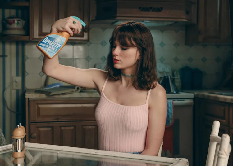 Swift spritzes her hair with a spray bottle marked "Opalite — Magical Results."