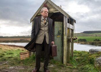Timothy Spall standing outside a run-down bus shelter in The Last Bus