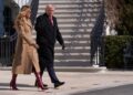 An individual dressed in a formal black coat accompanied by another person wearing a beige coat and red boots is walking in fron