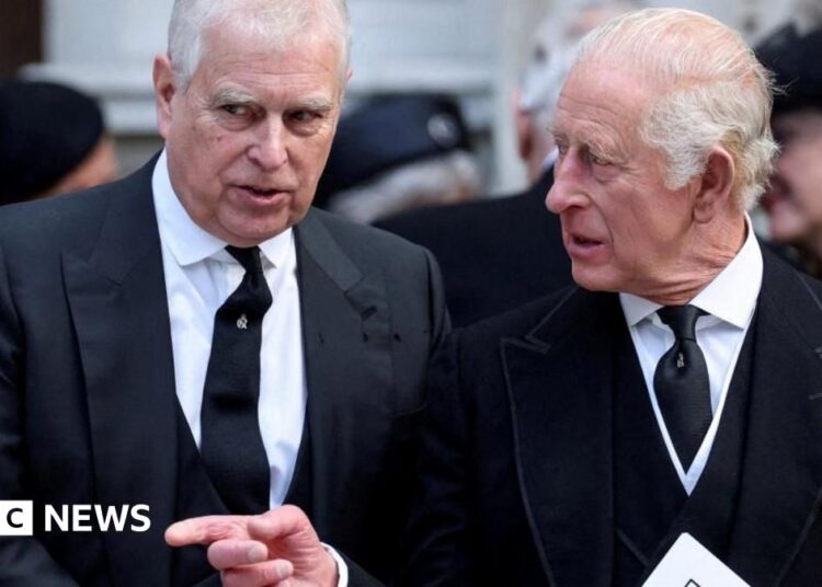 Andrew and King Charles talking as they walk. Charles points across Andrew and looks to the side while Andrew looks ahead. They both wear black suits, white shirts and black ties