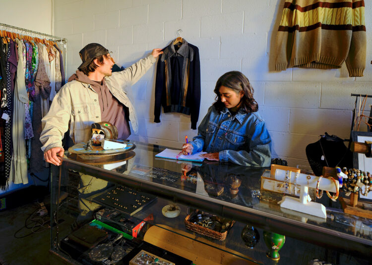 Seller Tristan hangs a jacket on the wall inside his vintage store