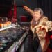 Photo of a man next to CDjs wearing a golden coat.